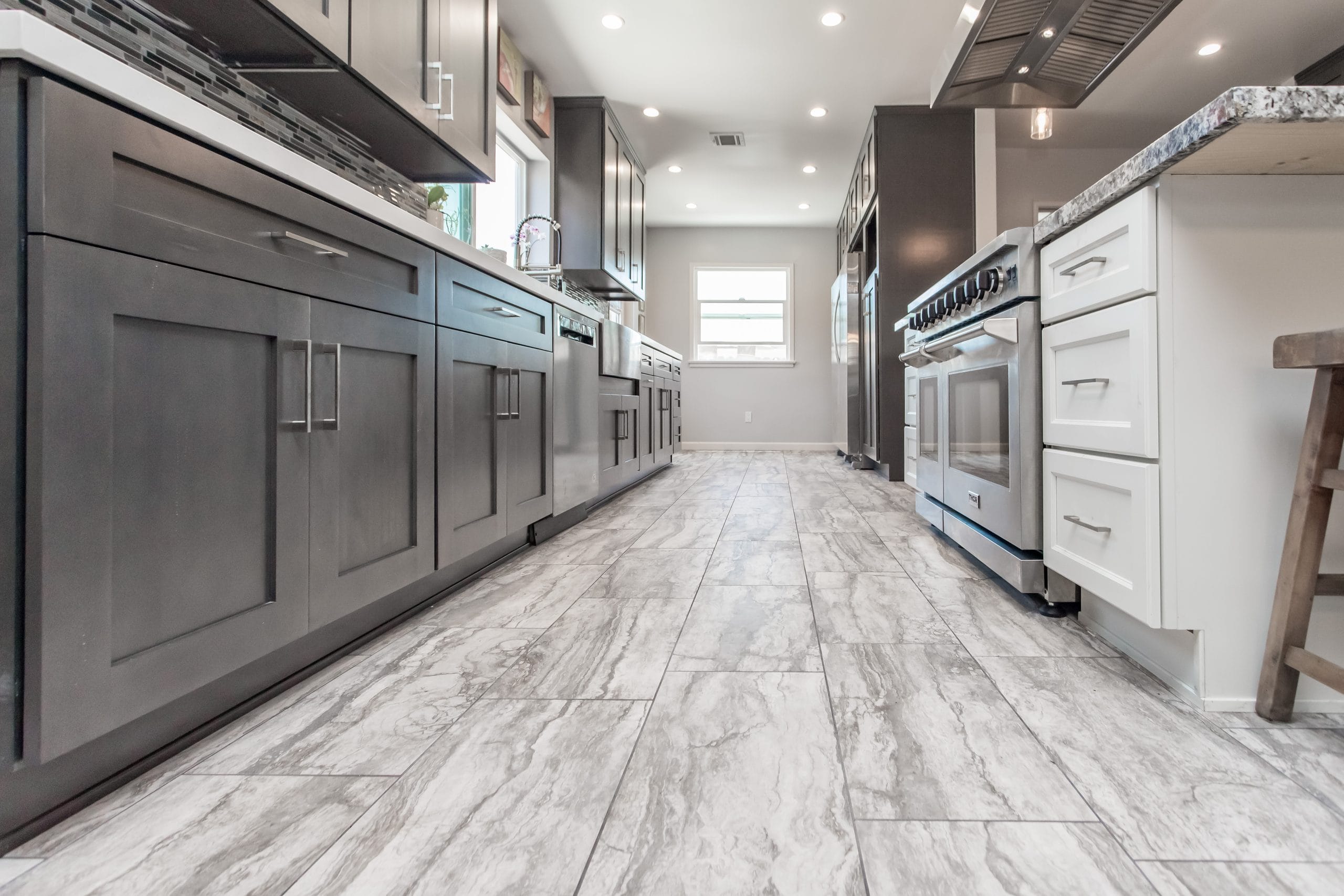 A long kitchen run in grey shaker cabinetry with a slide-in range, seen down the length of the marble-effect floor tile