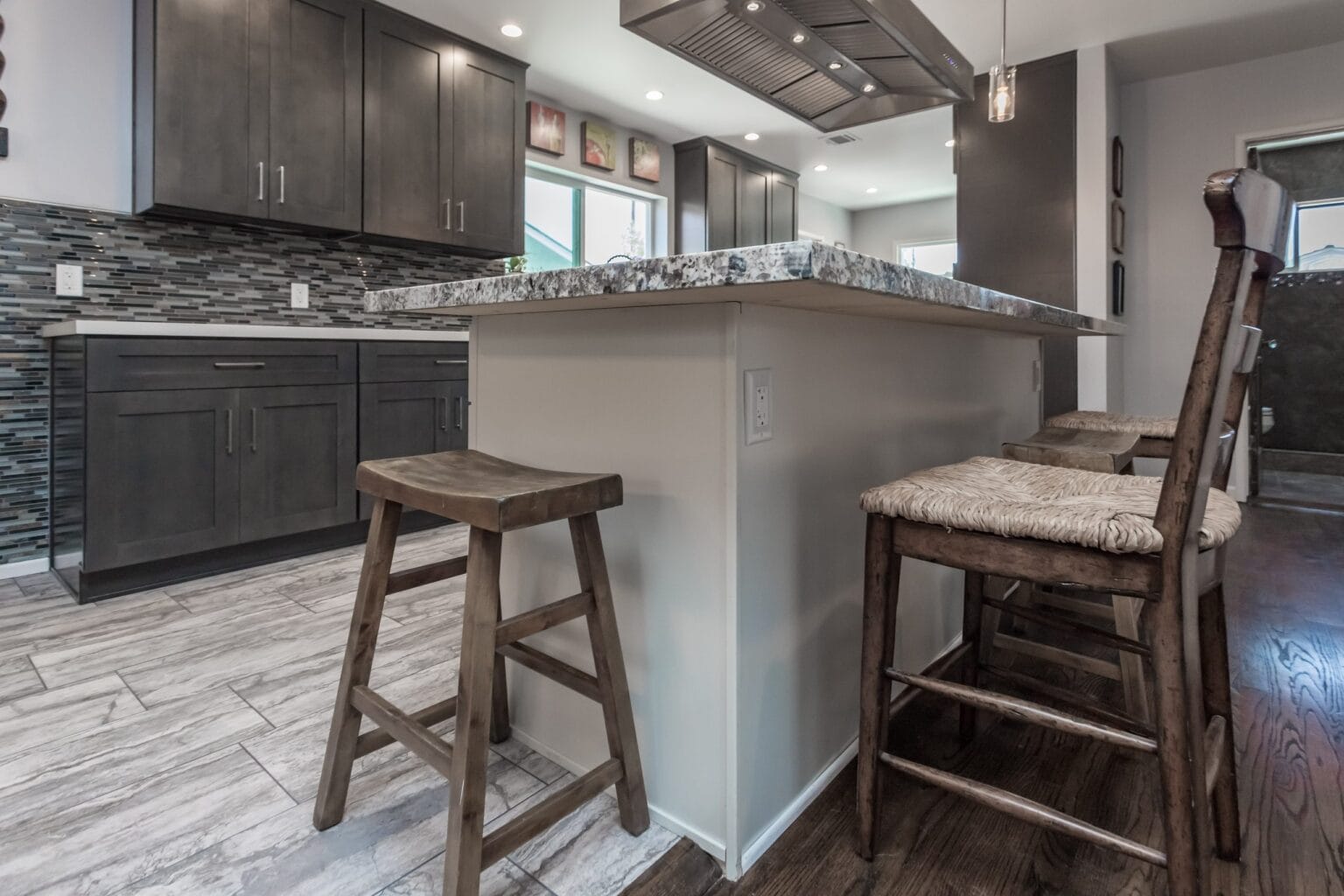 The end of the island with timber stools drawn up to the granite overhang, and grey shaker bases behind