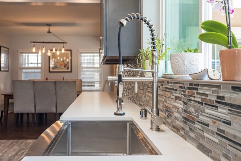 Undermount sink with a spring-neck tap against a linear mosaic splashback, looking through to the dining area, on an Elbaz Construction kitchen