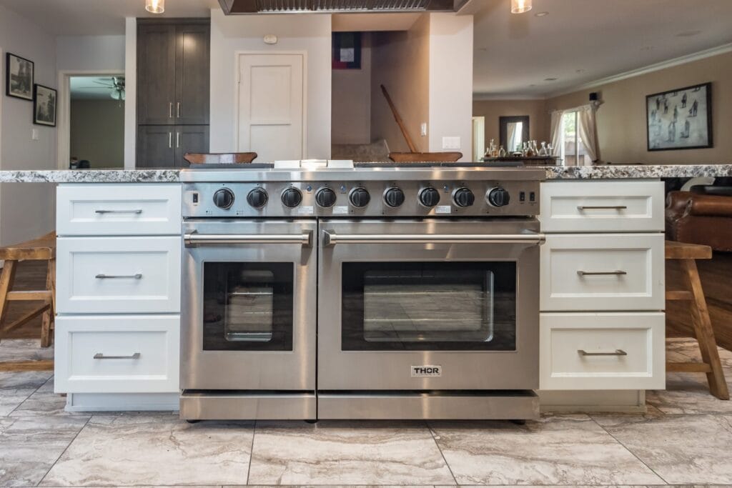 A wide double range set between white cabinetry under a granite worktop, on an Elbaz Construction kitchen remodel