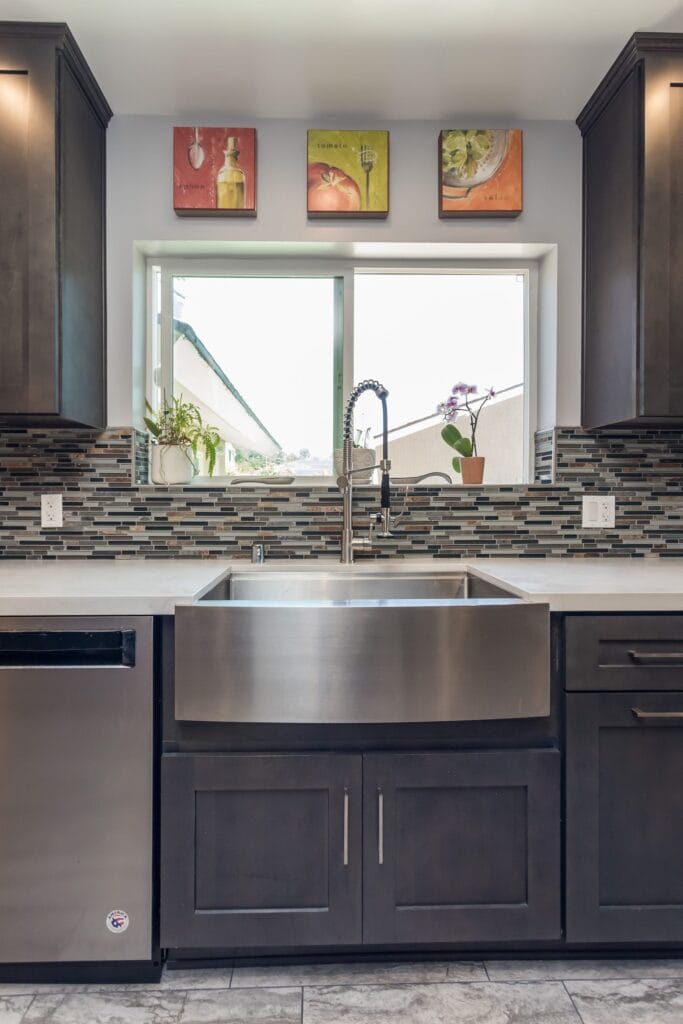 Stainless apron-front sink under a window in a grey shaker run with a mosaic splashback, by Elbaz Construction