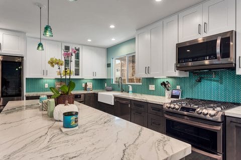 Kitchen remodel with marble counters, farmhouse sink and teal tile backsplash