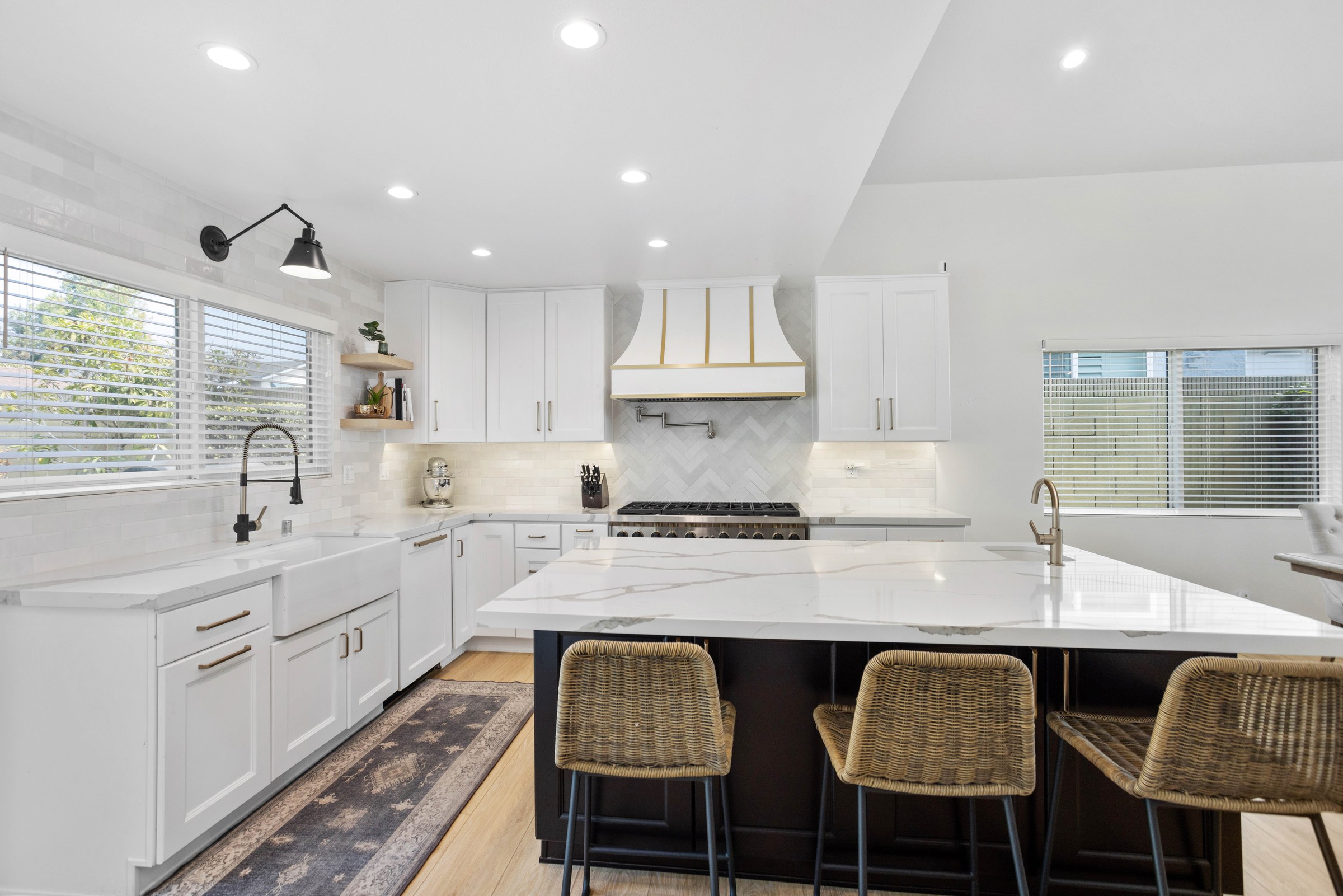 White shaker kitchen remodel with a brass-trimmed range hood, herringbone marble backsplash and a dark waterfall-edge island