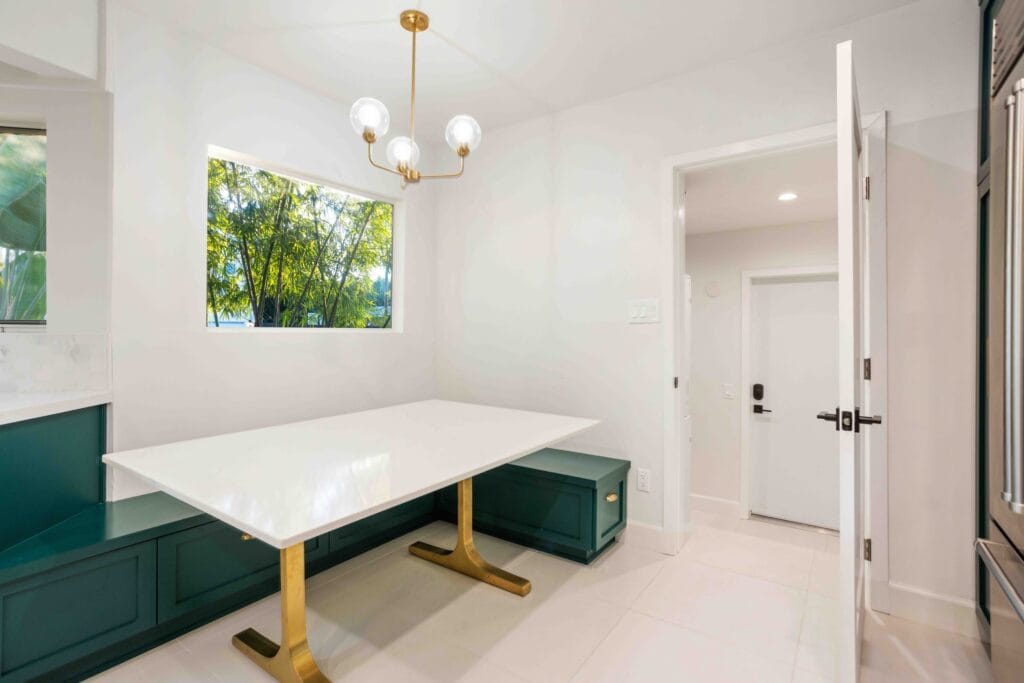 Cantilevered white table on a brass pedestal built into a teal banquette base, with a globe pendant above, by Elbaz Construction