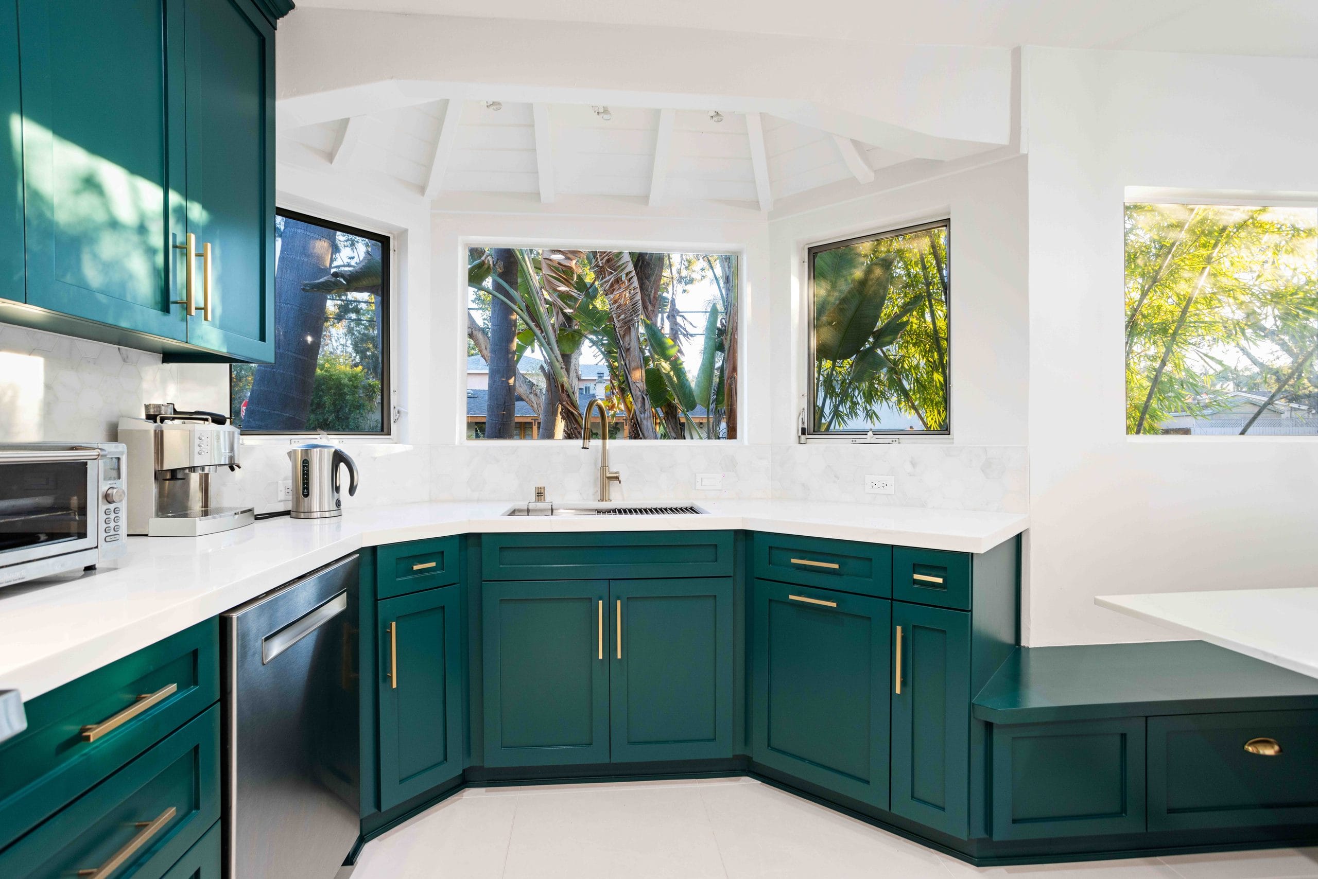 Teal shaker kitchen wrapping a corner of windows, with white quartz counters and a garden beyond