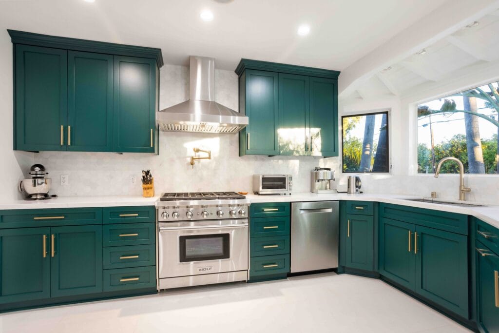 The same teal kitchen read along the run, with the range, extractor and integrated dishwasher set into a continuous white worktop, by Elbaz Construction
