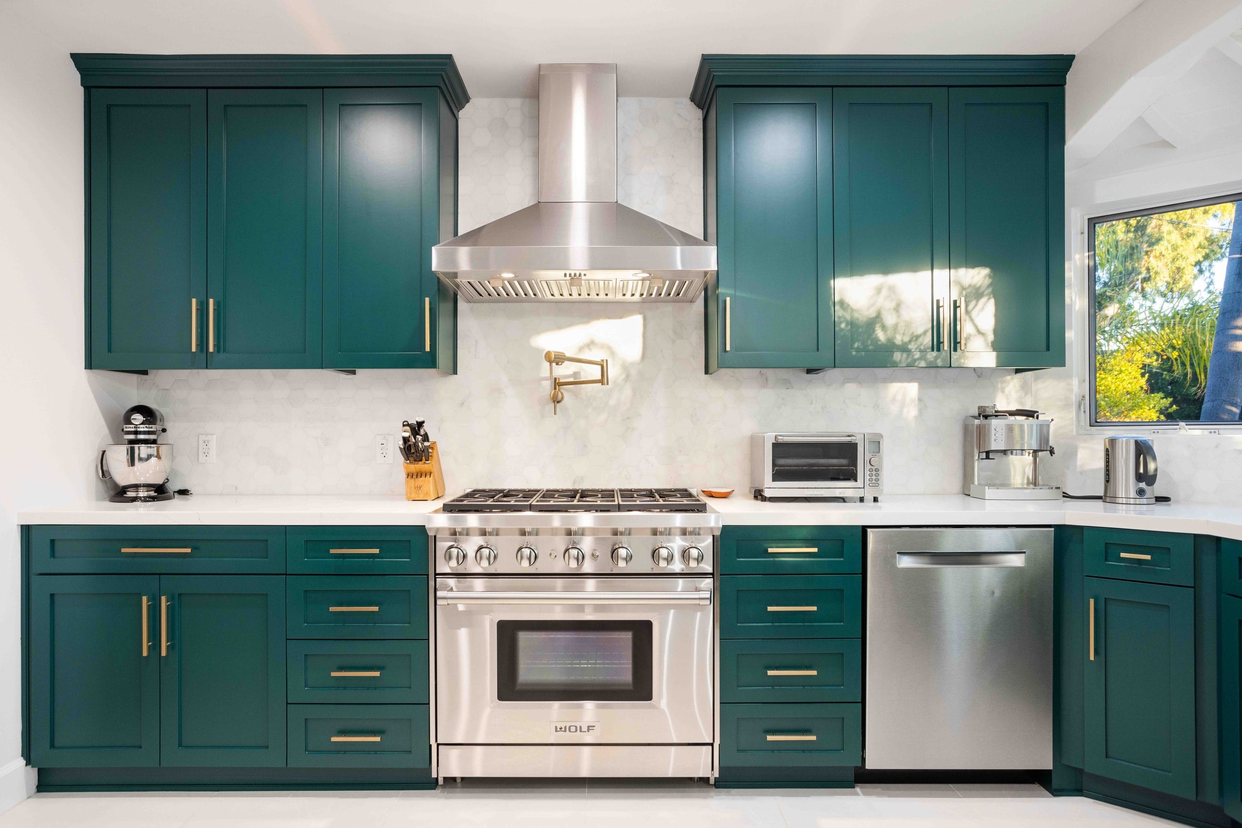 Teal shaker kitchen by Elbaz Construction with brass hardware, a professional range under a stainless chimney extractor and a marble-look splashback