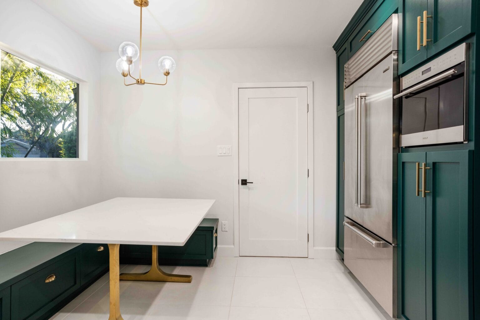 The same kitchen from the dining end, with the quartz table, brass pendant and the tall cabinetry run housing the fridge and ovens