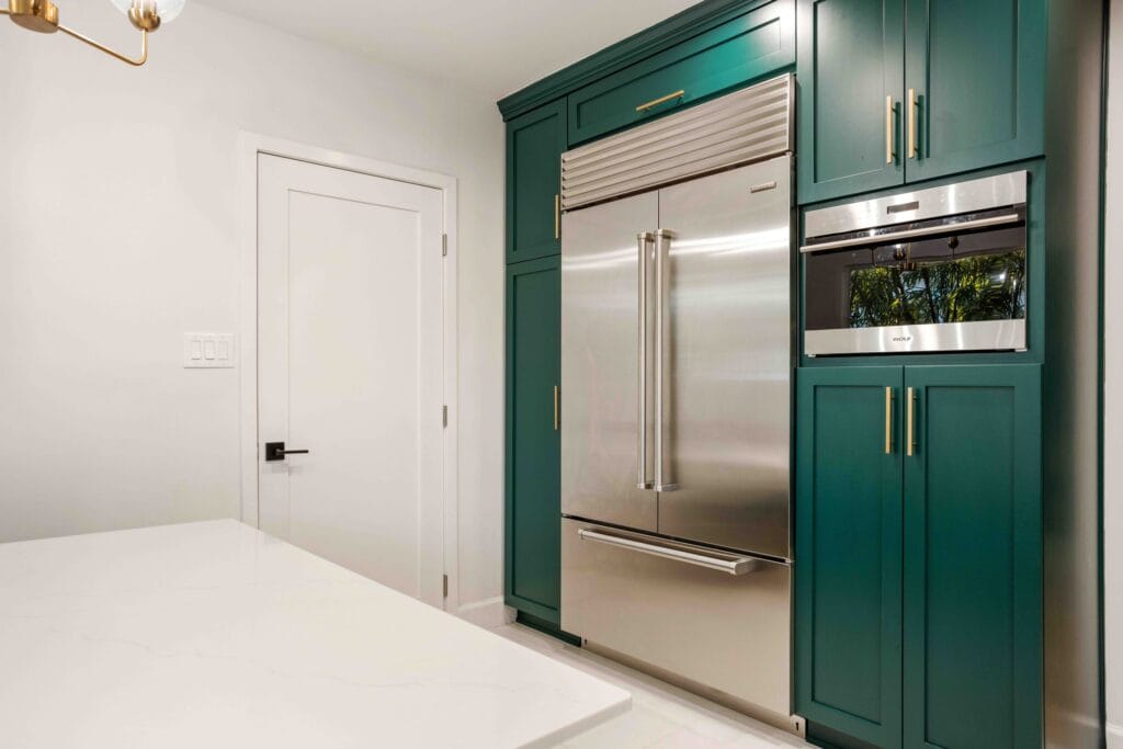Tall teal cabinetry housing an integrated fridge-freezer and a stacked oven and microwave, beside a white door and worktop return