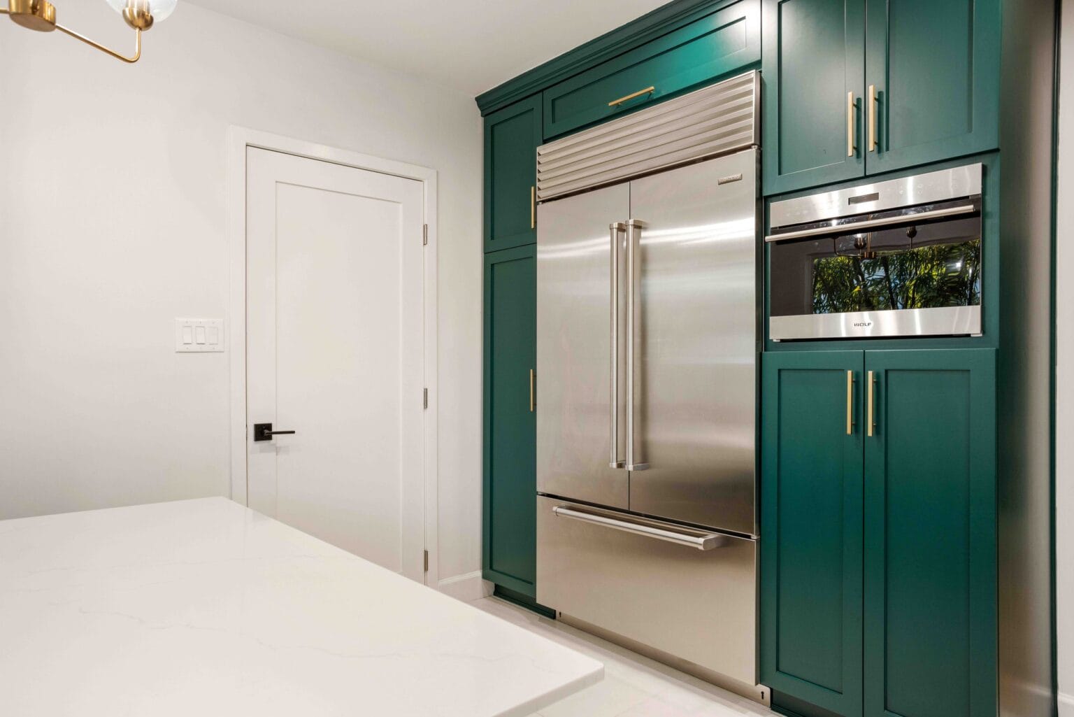 Tall teal cabinetry housing the fridge and a built-in oven, with the worktop run continuing past it