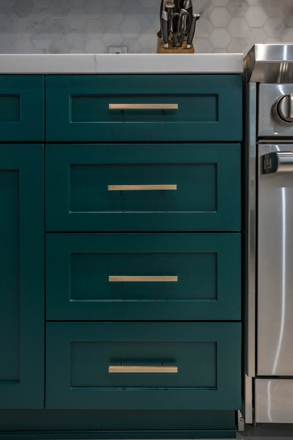Close detail of teal shaker drawer fronts with long brass bar handles, running up to a stainless range