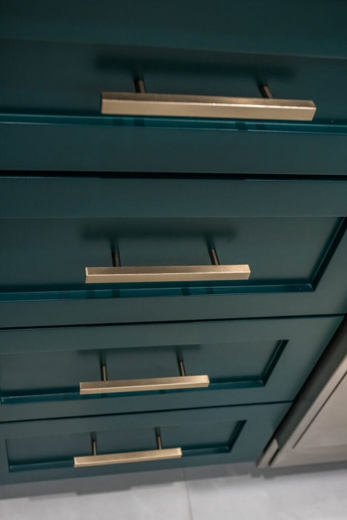 Detail of teal shaker drawer fronts and slim brass bar handles on an Elbaz Construction kitchen