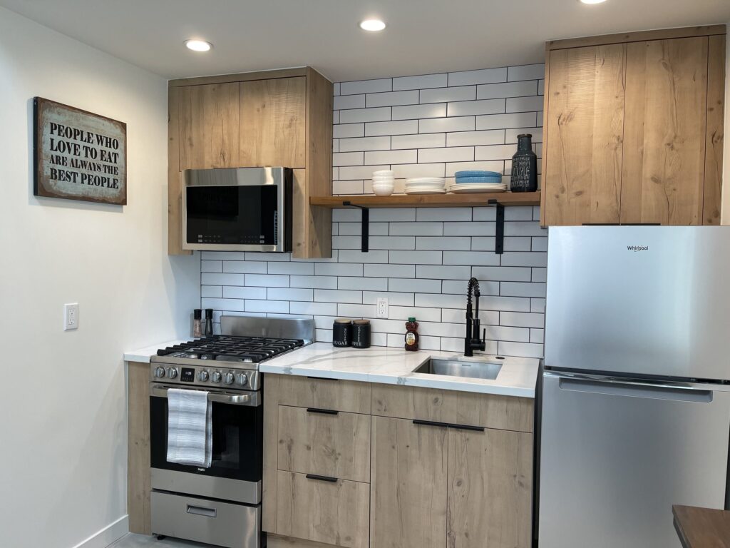 A larger two-storey ADU by Elbaz Construction with a loft bedroom, full kitchen and laundry, shown for scale against a studio unit