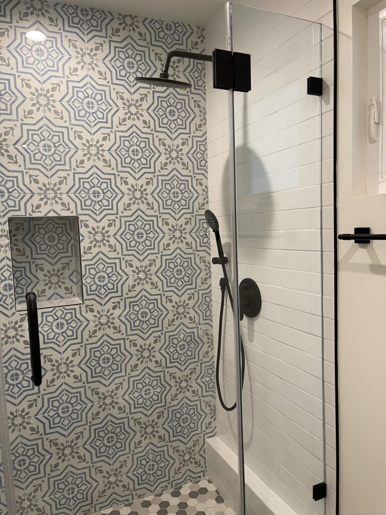 Shower enclosure in a loft accessory dwelling lined in patterned encaustic-style tile with a matt-black rain head and recessed niche