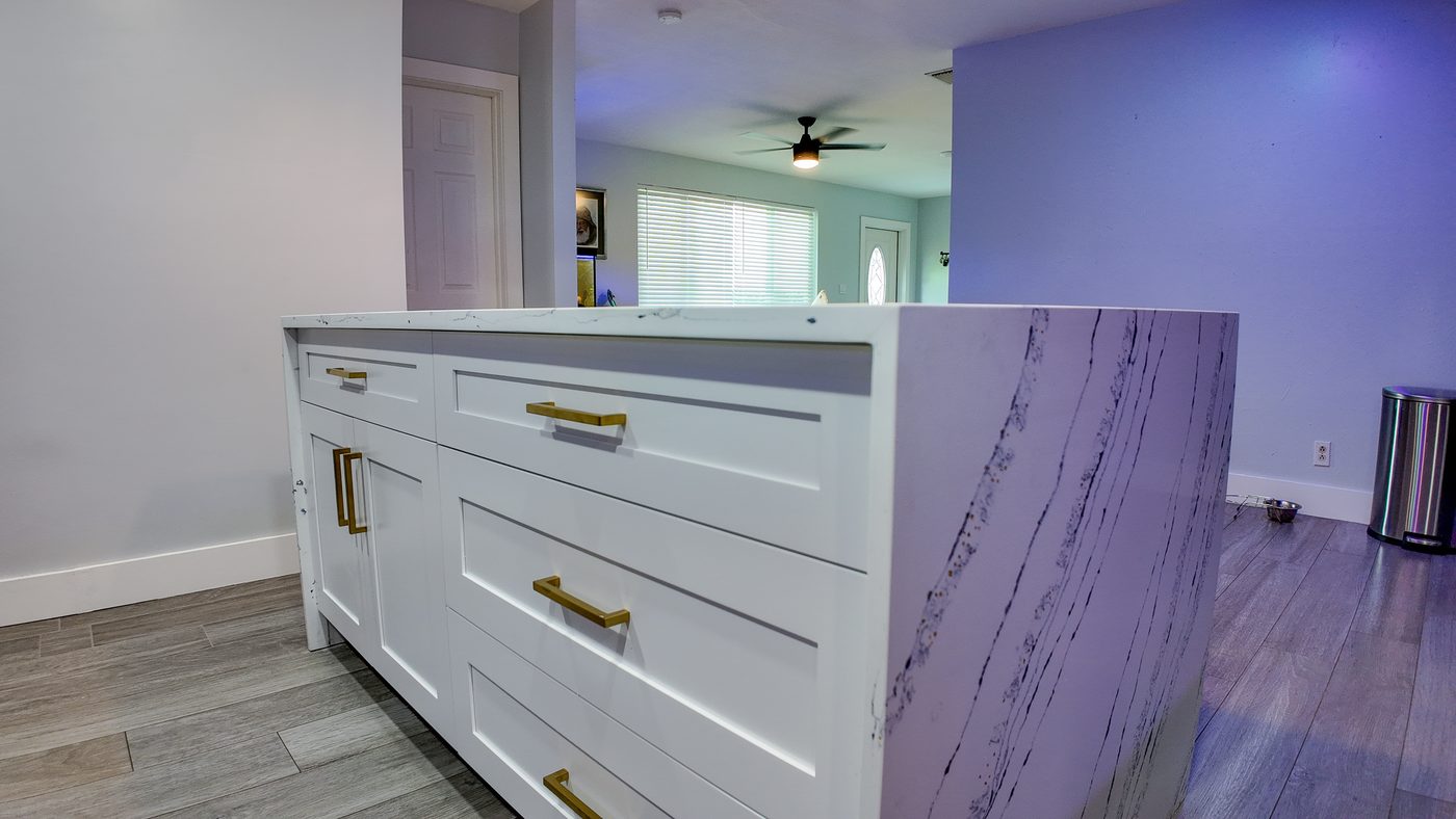 Waterfall end of a white quartz island with grey veining above pale plank flooring
