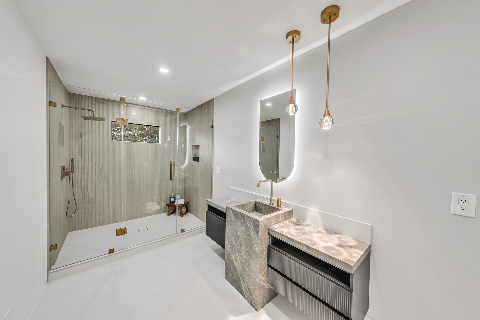 Luxury bathroom vanity with marble pedestal sink, brass pendant lighting and backlit mirror