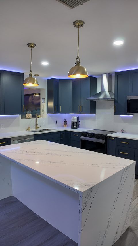 Navy and brass kitchen with waterfall quartz island and LED accent lighting