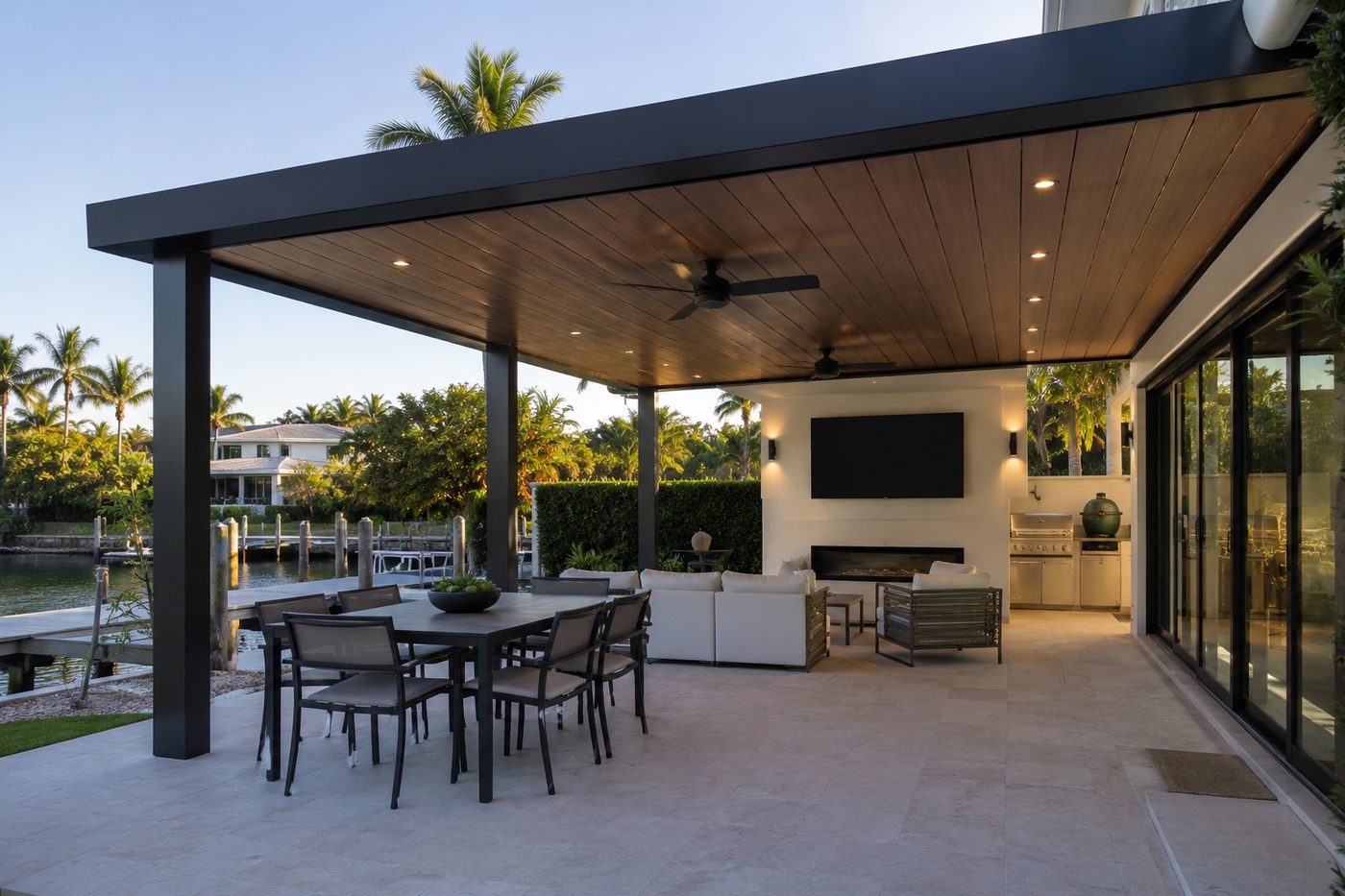 Covered outdoor kitchen and dining area with a built-in grill run overlooking the water, built by Elbaz Construction