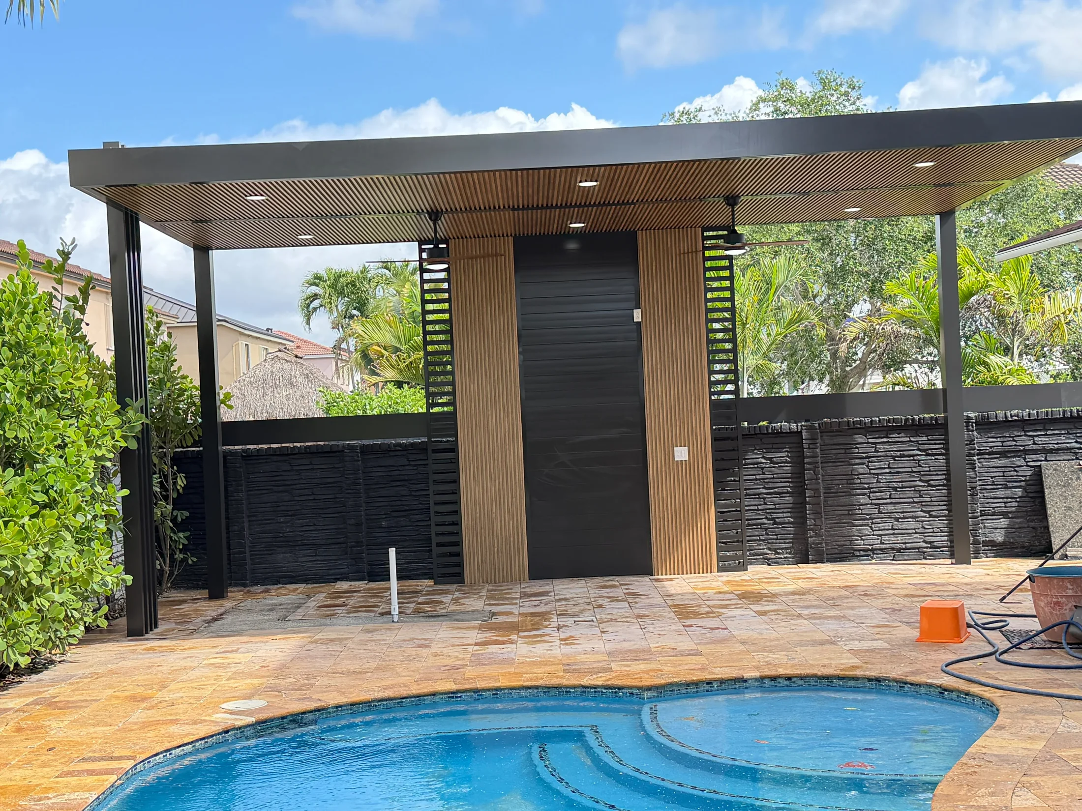 Dark-framed pergola over a travertine deck with a built-in outdoor kitchen and dining seating