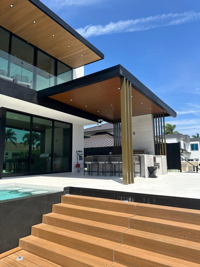 Timber-faced steps rising from a pool deck to a covered terrace, with the columns and soffit above, by Elbaz Construction
