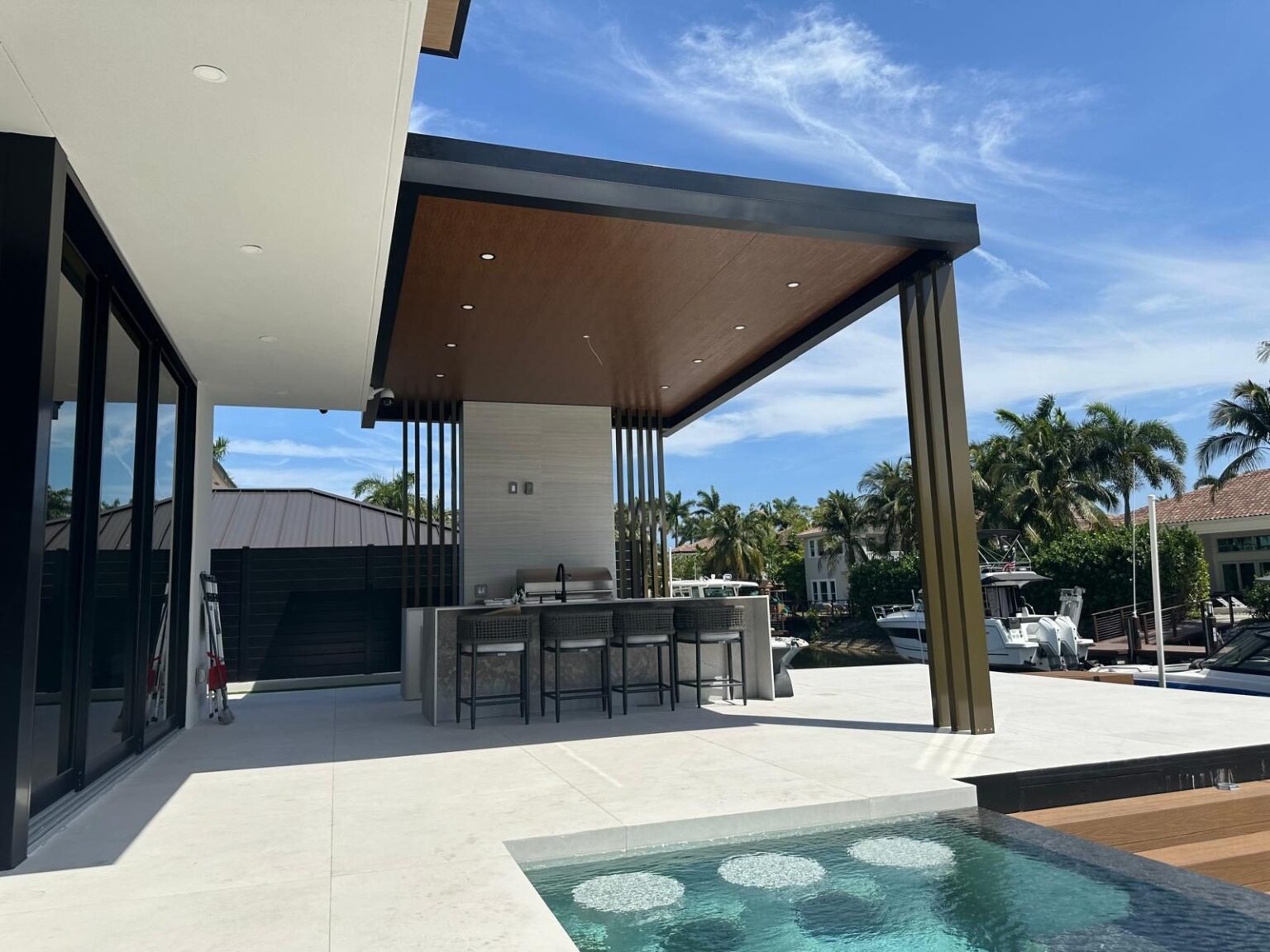 The covered terrace and outdoor kitchen counter beside the pool, with the deck finished in pale paving