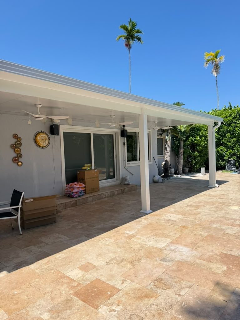 A white aluminium patio cover carried on posts over a travertine terrace, running along the rear of a single-storey home