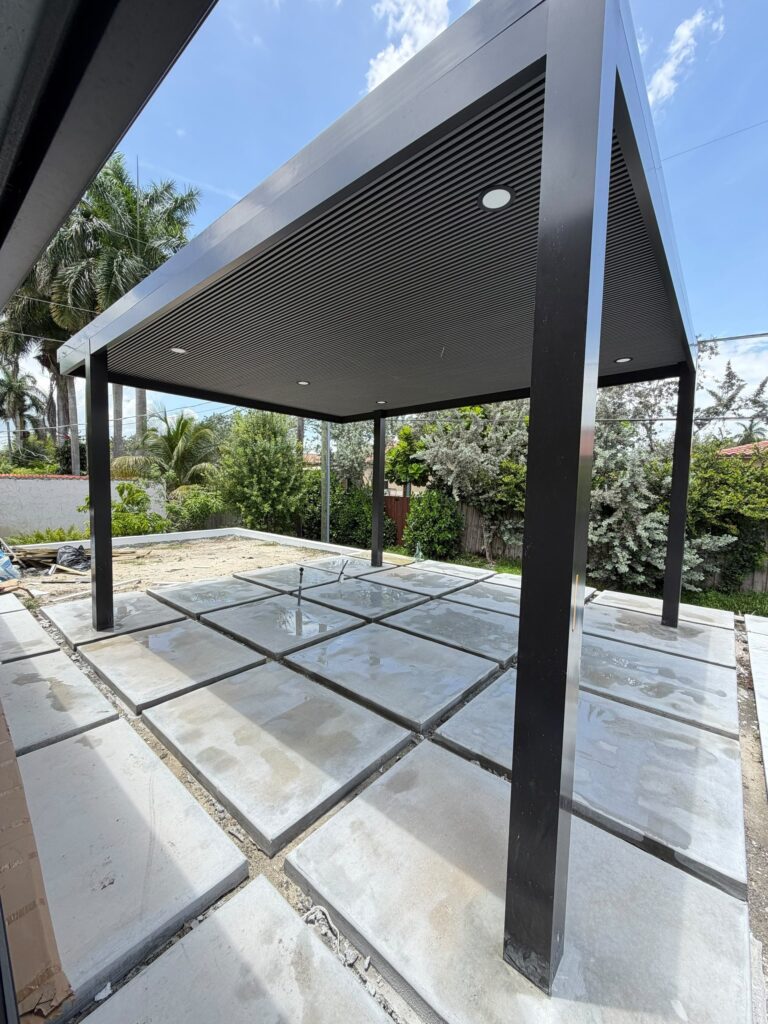 Freestanding louvred pergola standing over a large-format paver pool deck part way through installation