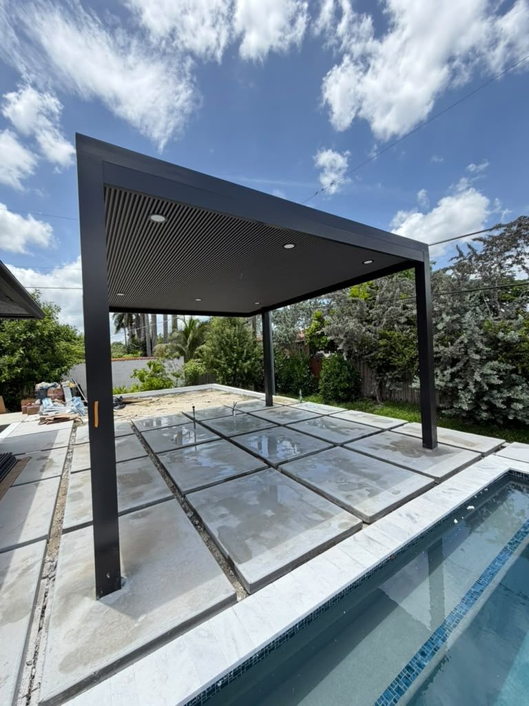 The same louvred pergola from the pool side, with paving stacked and the deck still being set