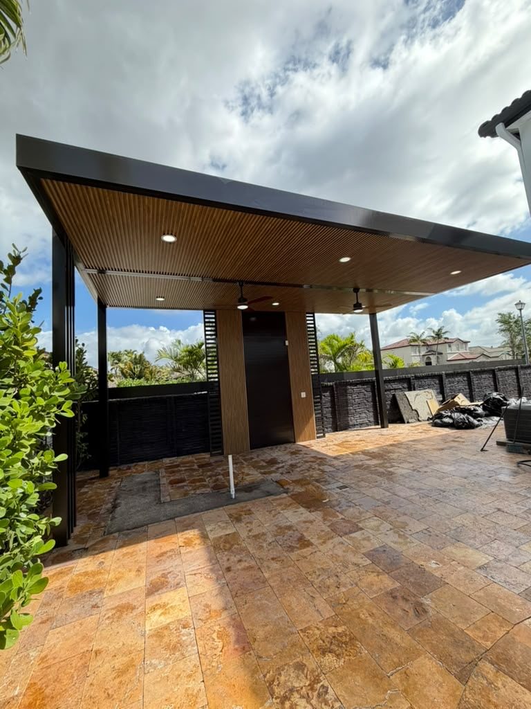A finished covered terrace with a dark timber-lined soffit on slim columns, over a travertine deck
