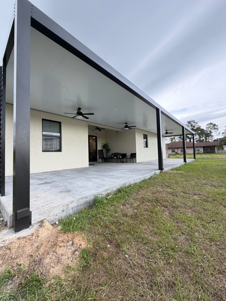 Long attached cover running the width of a house over a poured concrete slab, with the ground alongside not yet reinstated
