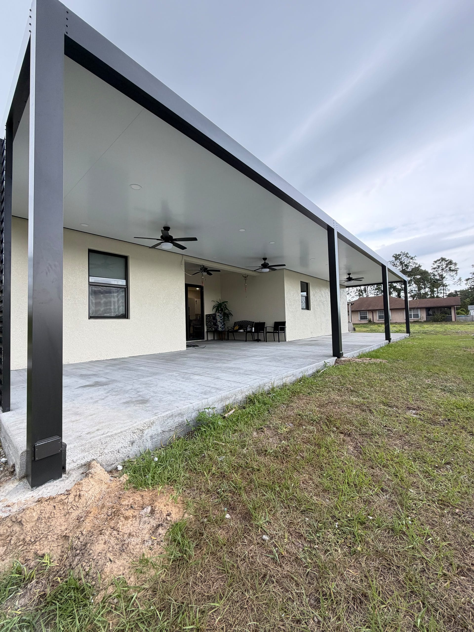 Long white patio cover with ceiling fans running along a cream stucco elevation, the ground not yet reinstated