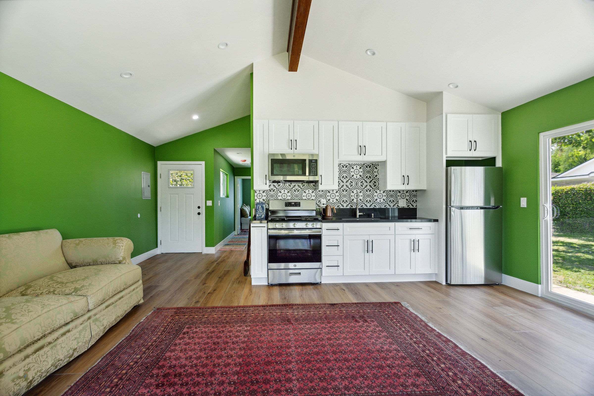 Detached room addition with a vaulted beamed ceiling, white kitchen and patterned tile backsplash