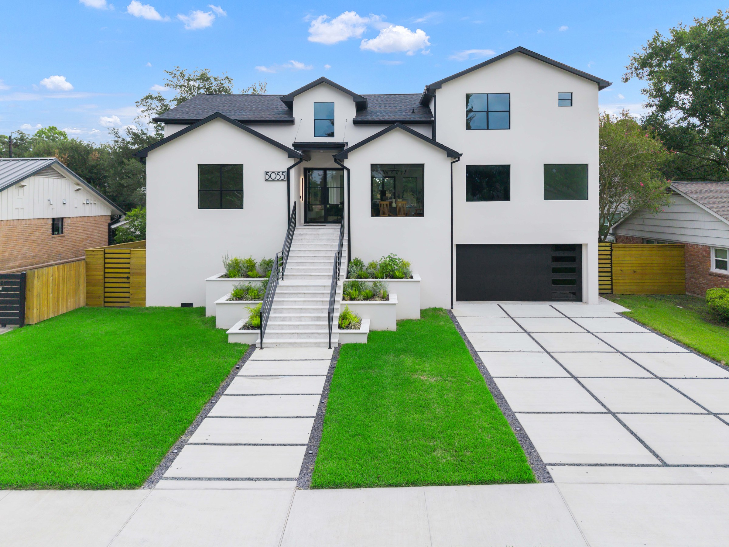 White two-story modern farmhouse in South Florida with black-framed windows and a landscaped entry stair, completed by Elbaz Construction