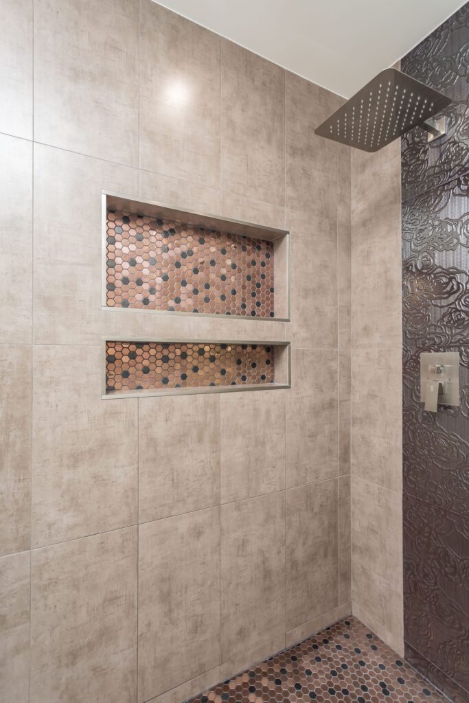 Compact bathroom remodel by Elbaz Construction with a walk-in shower, copper-tone penny mosaic niches and floor, textured feature tile and a dark vanity with a stone top