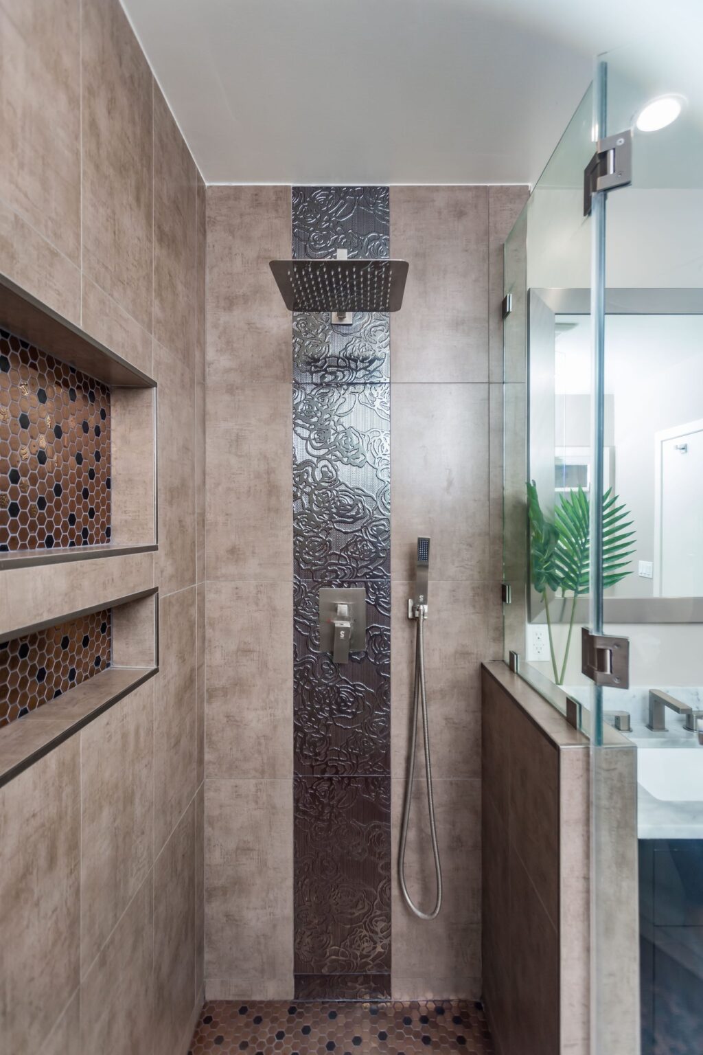 Walk-in shower by Elbaz Construction with a rain head, a textured feature tile band and copper-toned mosaic shelves set into the wall