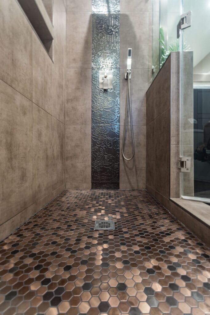 Compact bathroom remodel by Elbaz Construction with a walk-in shower, copper-tone penny mosaic niches and floor, textured feature tile and a dark vanity with a stone top