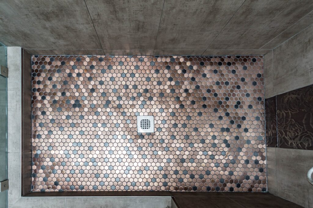 Compact bathroom remodel by Elbaz Construction with a walk-in shower, copper-tone penny mosaic niches and floor, textured feature tile and a dark vanity with a stone top