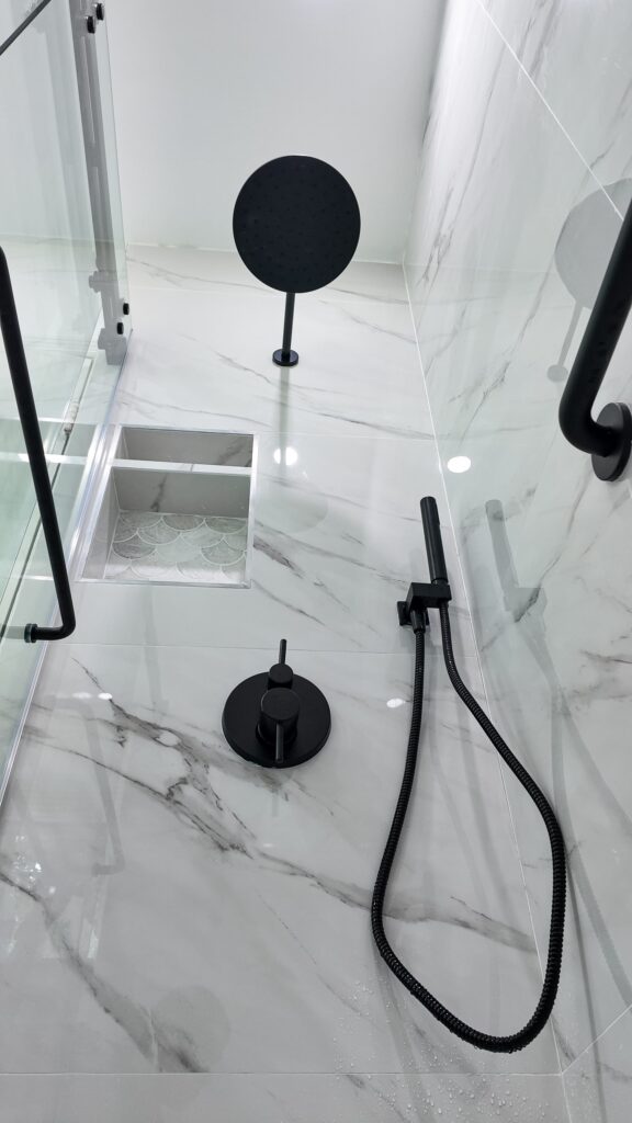 Compact bathroom remodel by Elbaz Construction with large-format marble-look porcelain, a fish-scale mosaic shower floor, matte black fixtures and a fluted oak vanity