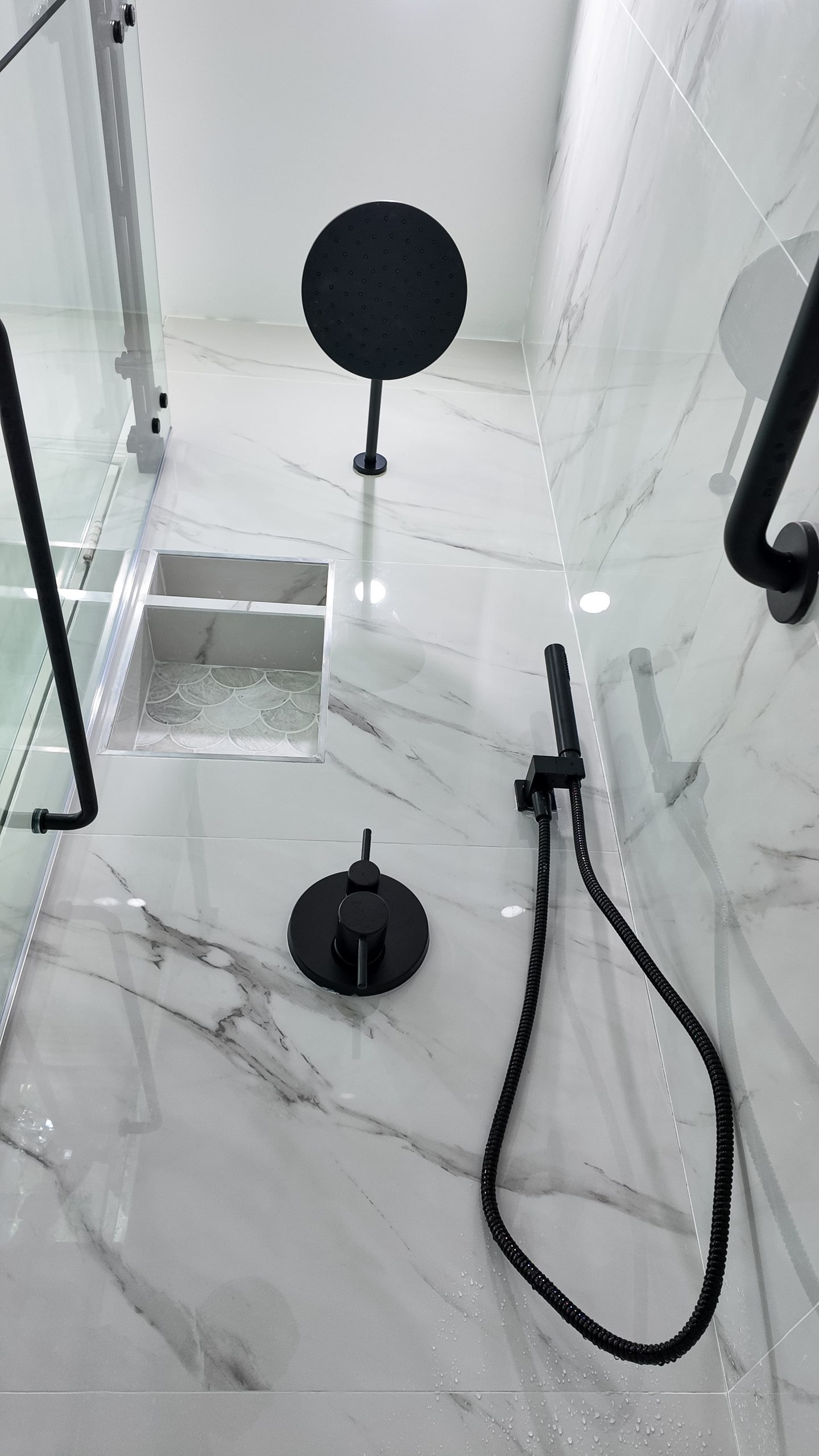 Walk-in shower by Elbaz Construction lined in large-format marble-look porcelain with matte black fixtures and a linear drain