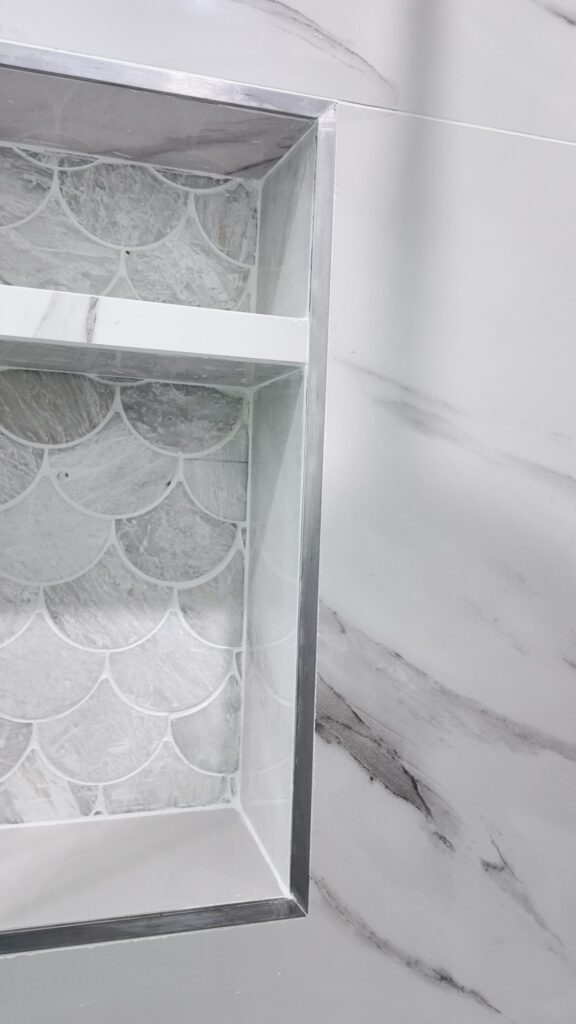 Compact bathroom remodel by Elbaz Construction with large-format marble-look porcelain, a fish-scale mosaic shower floor, matte black fixtures and a fluted oak vanity