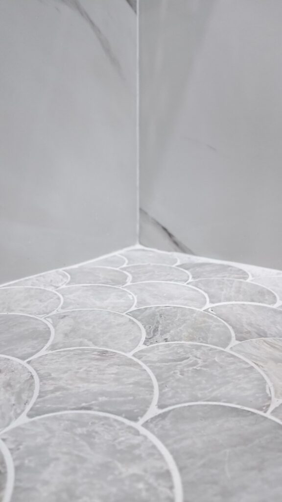 Compact bathroom remodel by Elbaz Construction with large-format marble-look porcelain, a fish-scale mosaic shower floor, matte black fixtures and a fluted oak vanity