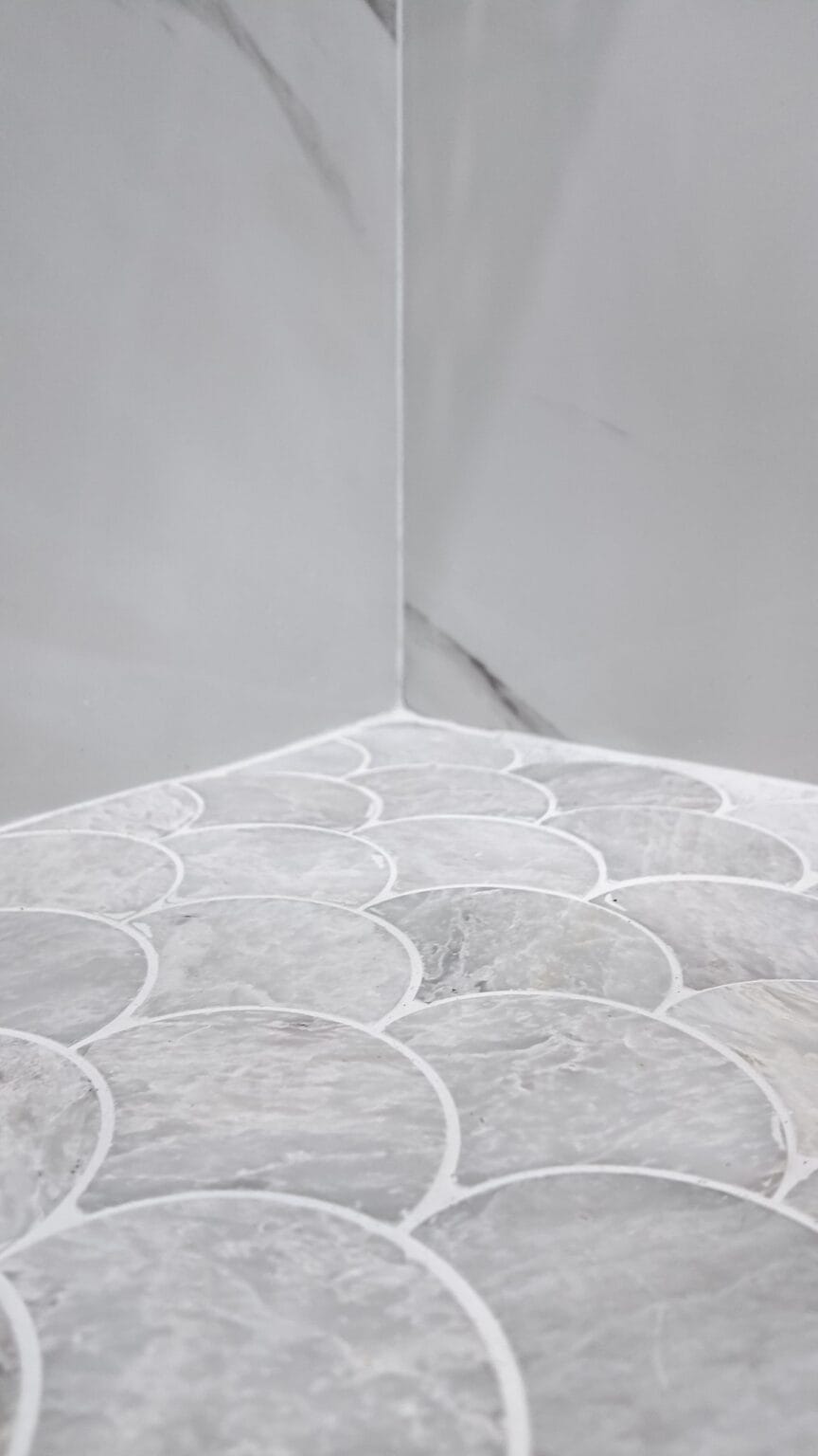 Fan-shaped mosaic floor tile meeting the marble-look wall tile in the corner of a walk-in shower