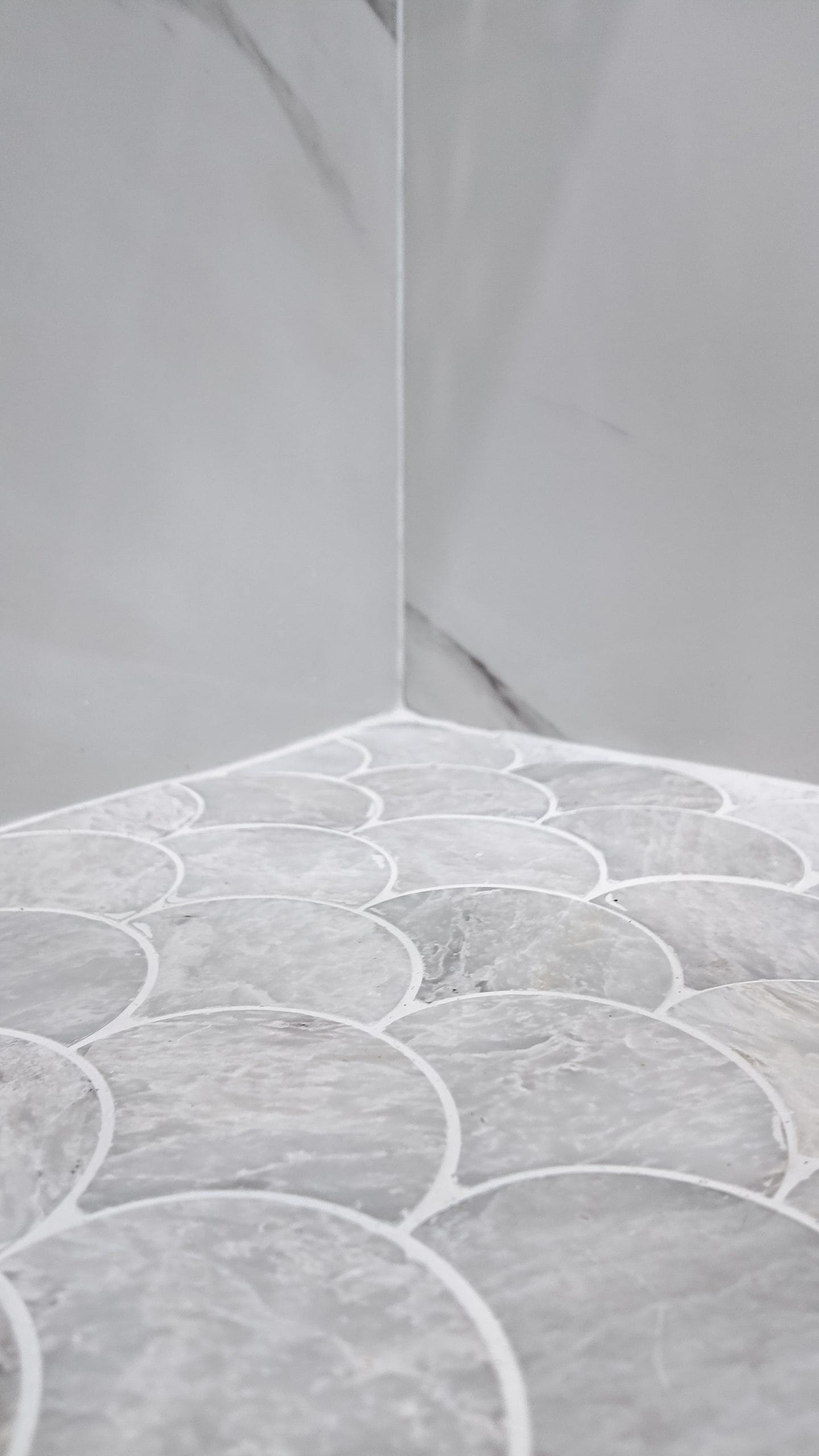 Fan-shaped mosaic floor meeting the marble-look wall tile in the corner of the shower