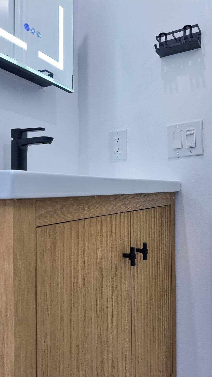The vanity from the side, with the black mixer, the fluted oak door and the switch and socket plates set into the wall
