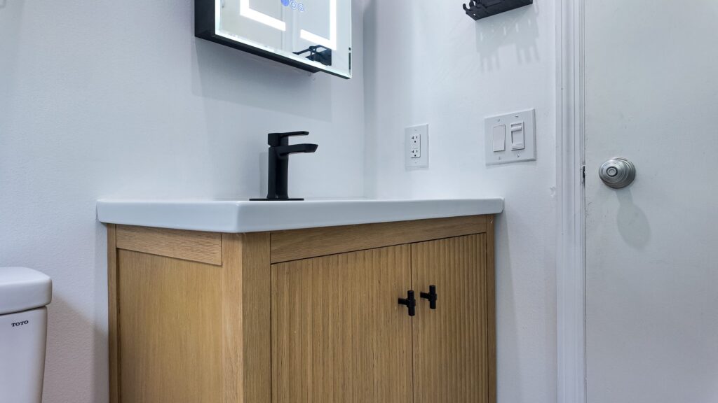 Compact bathroom remodel by Elbaz Construction with large-format marble-look porcelain, a fish-scale mosaic shower floor, matte black fixtures and a fluted oak vanity