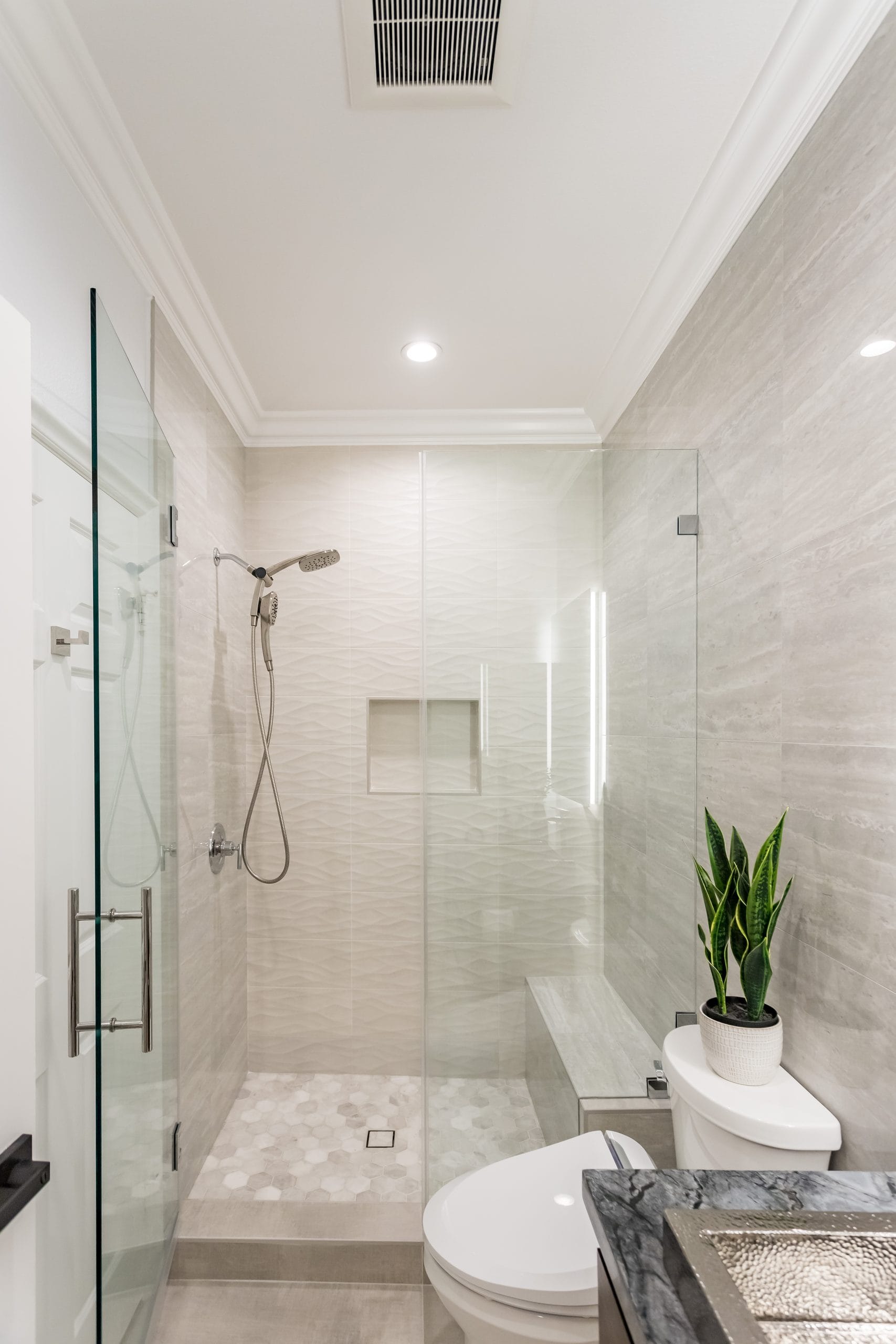 The narrow bathroom end to end: glass shower screen, tiled bench and the vanity in the foreground