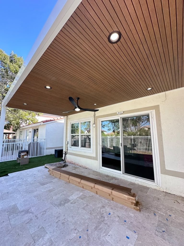 Patio cover with a timber-lined soffit and downlights over new travertine paving, beside a run of sliding doors