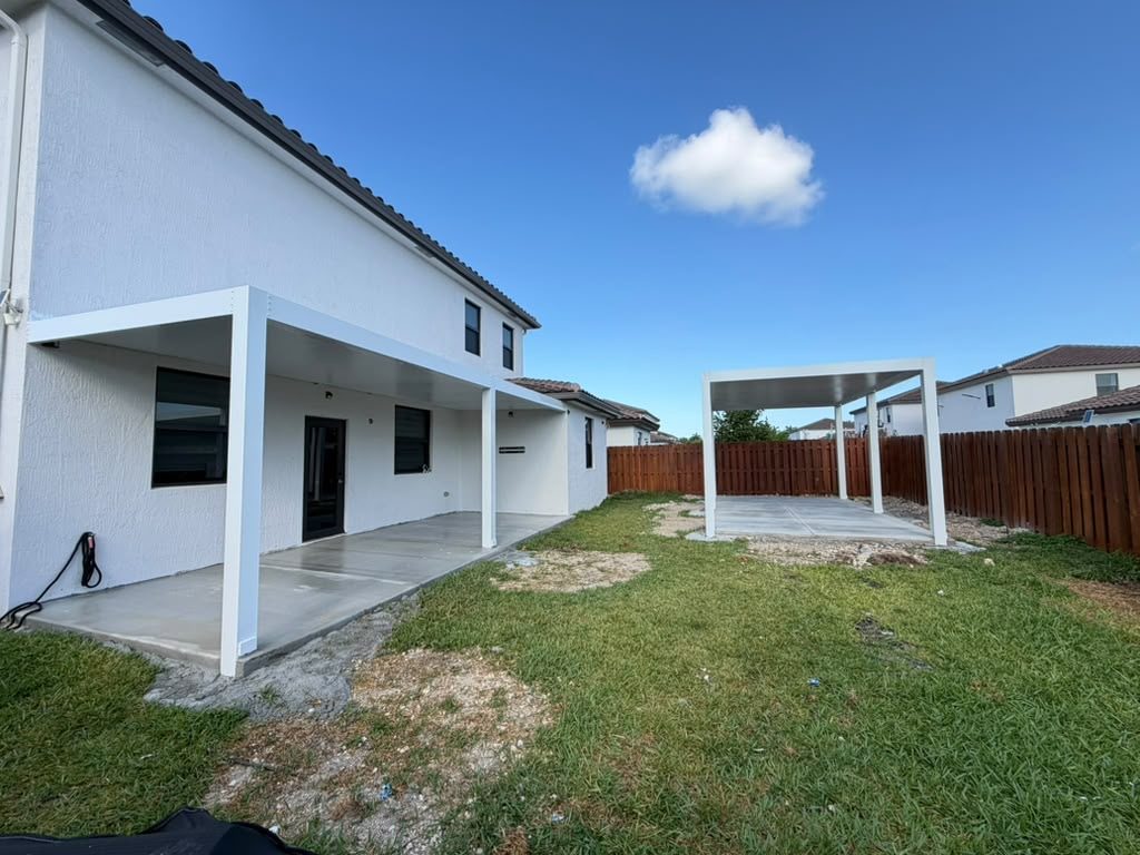 Wider view of the same rear elevation, showing the covered porch and a separate freestanding cover at the boundary