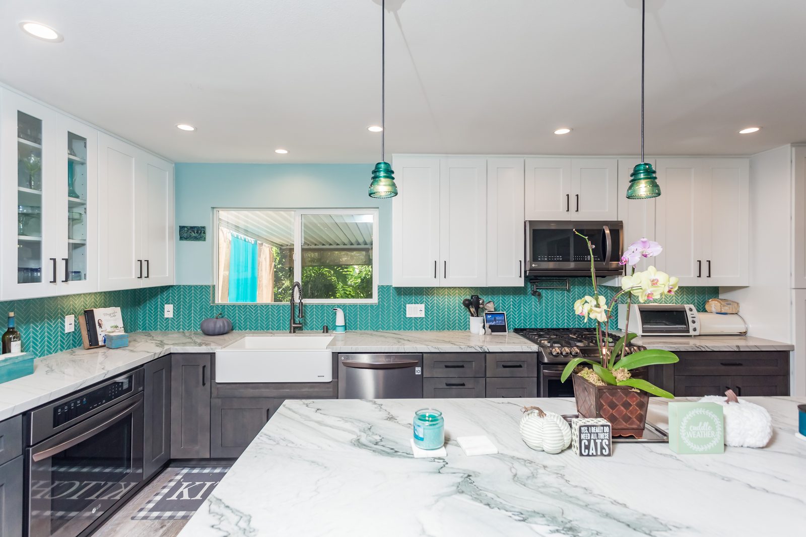 Kitchen with teal herringbone backsplash, farmhouse sink and marble island