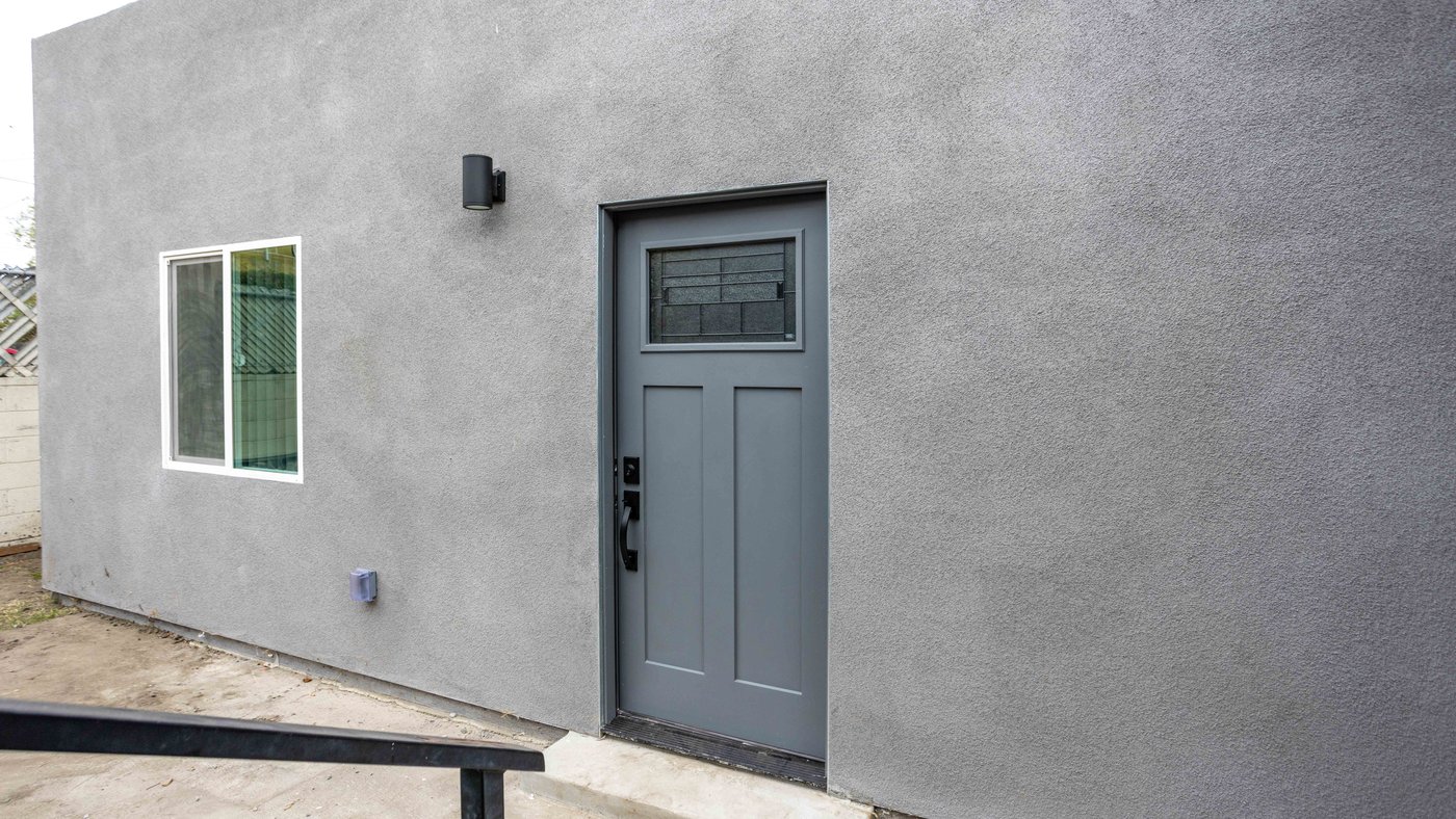 Completed garage-to-ADU conversion with a new entry door and window set where the vehicle opening was, finished in continuous stucco